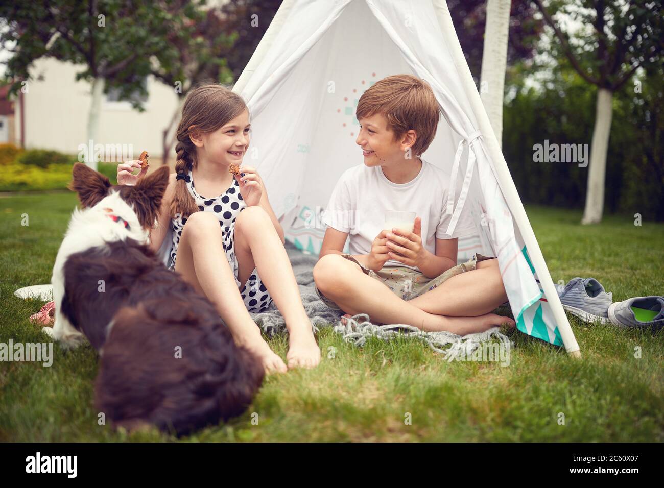 Sorridendo i bambini che giocano in cortile con il cane in teepee e mangia biscotti. Foto Stock