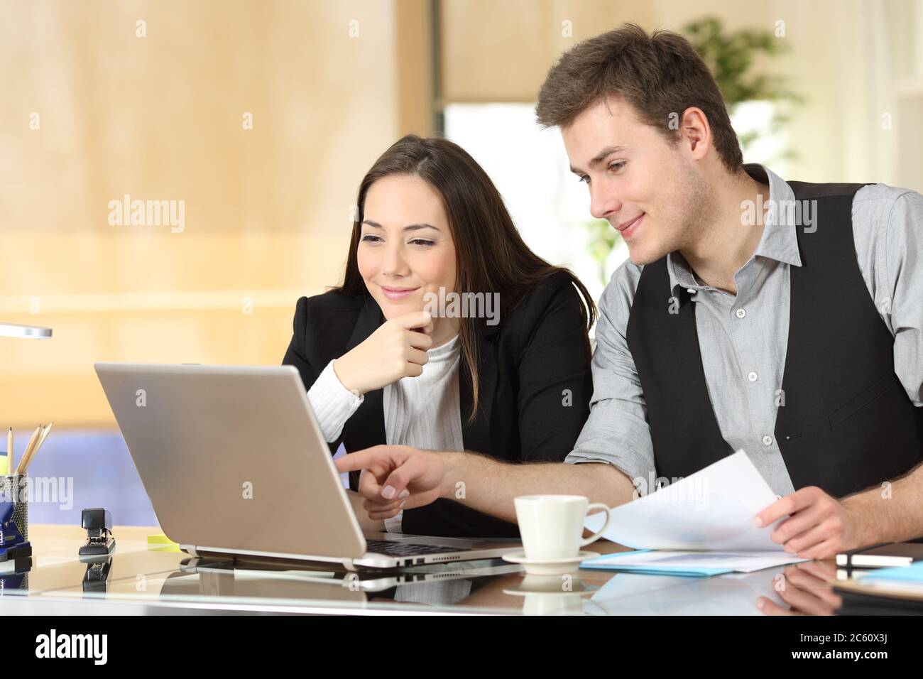 Impiegati soddisfatti che controllano i contenuti online dei notebook in ufficio Foto Stock