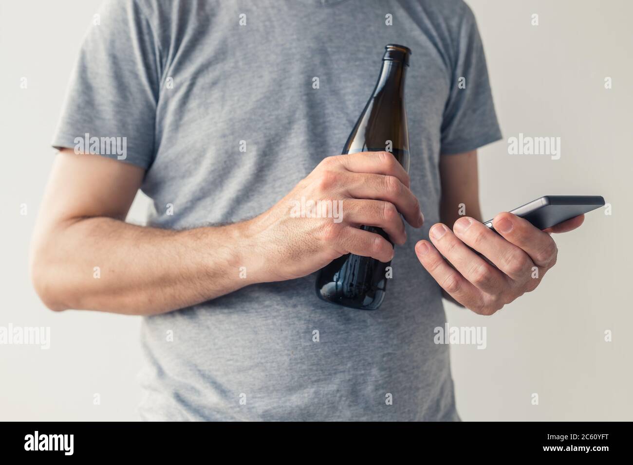 Bere birra e utilizzare lo smartphone, primo piano delle mani maschili con messa a fuoco selettiva Foto Stock