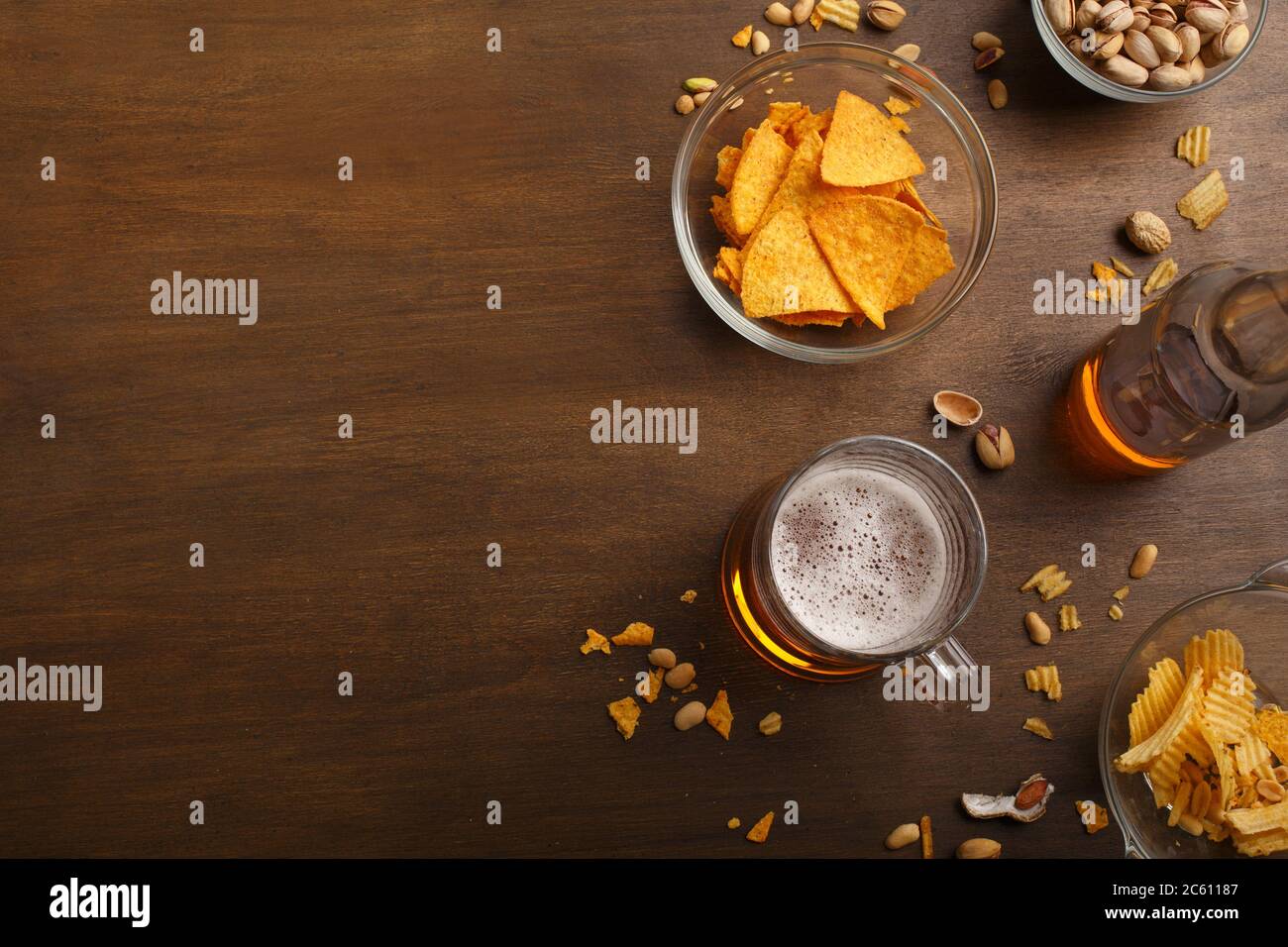 Tavolo del cliente in pub. Bicchiere di birra e bottiglia, nachos, patatine e pistacchi in piatti e sparsi Foto Stock