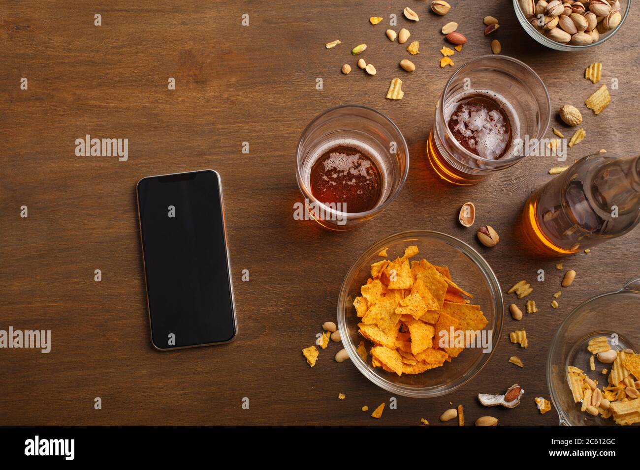 Incontri moderni al bar. Smartphone, due bicchieri di birra, bottiglia, pistacchio e patatine sono sparsi sul tavolo Foto Stock
