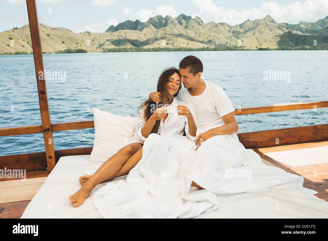 Felice giovane coppia innamorata di svegliarsi e gustare un caffè mattutino in barca in un tour privato in crociera. Letto a bordo. Viaggi e libertà di vita. Foto Stock