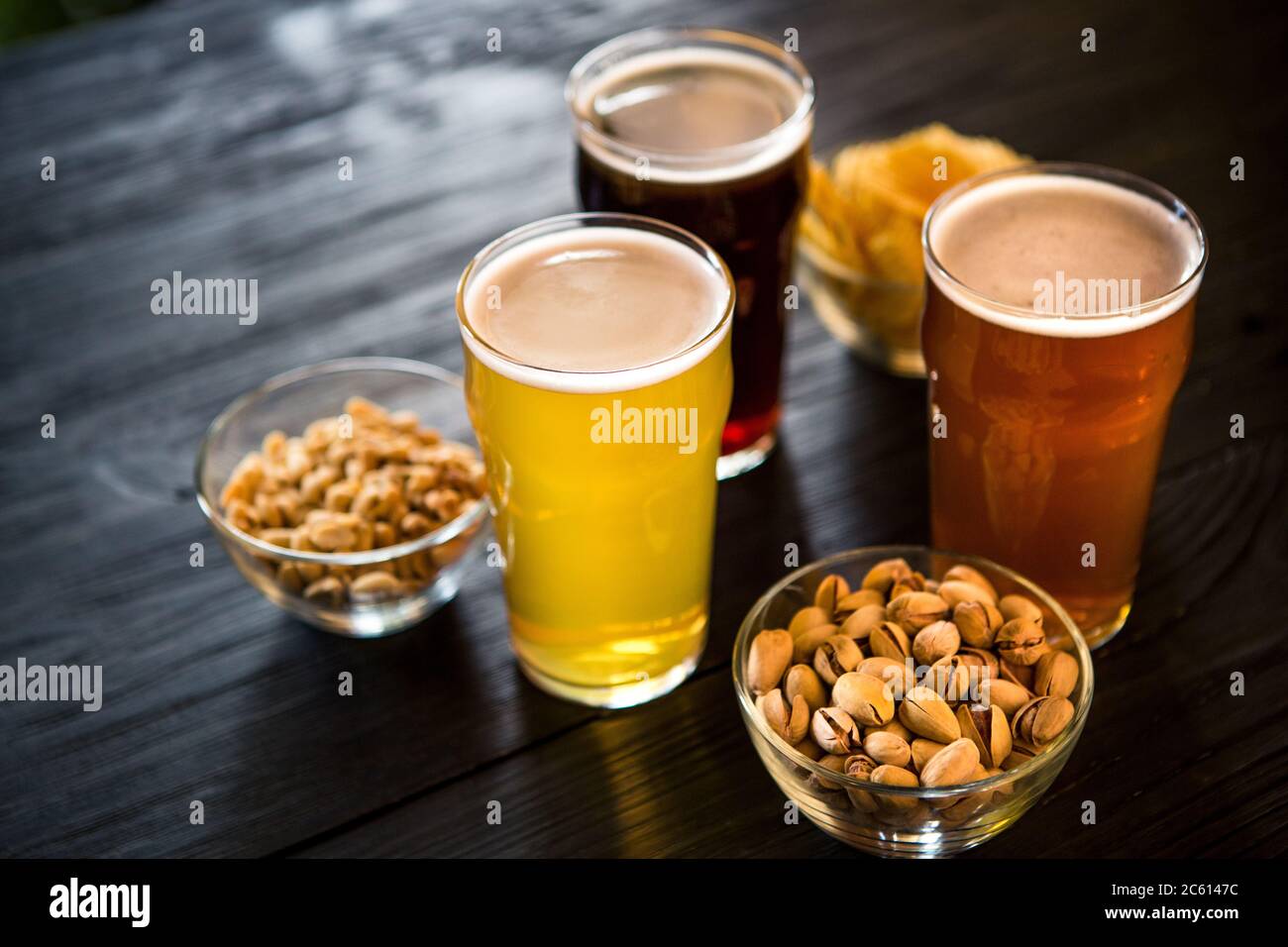 Bicchieri con tre tipi diversi di birra. Noci, fette biscottate e patatine in ciotole su tavola di legno Foto Stock