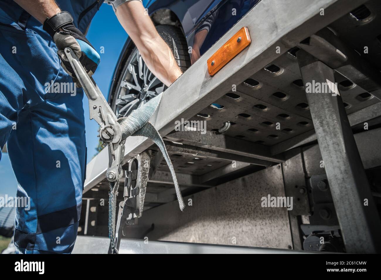 Lavoratore caucasico che fissa l'auto al traino di un autocarro utilizzando le cinghie di ancoraggio. Trasporto e tema Cargo. Foto Stock
