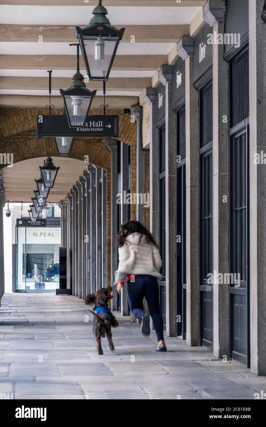 Regno Unito, Londra, West End. Una giovane donna e il suo cane da compagnia giocano in un chiostro in un'area vuota del mercato di Covent Garden, negozi chiusi, durante Covid-19 Foto Stock