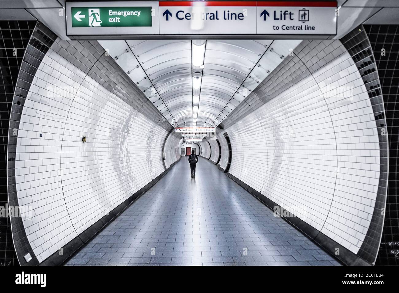 Una donna che cammina lungo un passaggio vuoto in una stazione sulla Central Line del sistema metropolitano di Londra Foto Stock