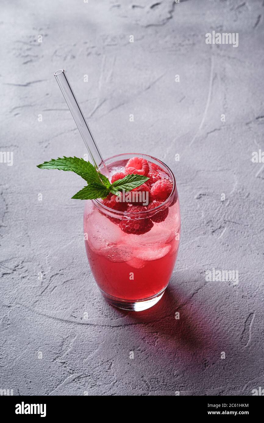 Bevanda fresca di succo di frutti di bosco ghiacciato con menta, limonata estiva di lamponi in vetro con cannucce su fondo in pietra e cemento, vista angolare Foto Stock