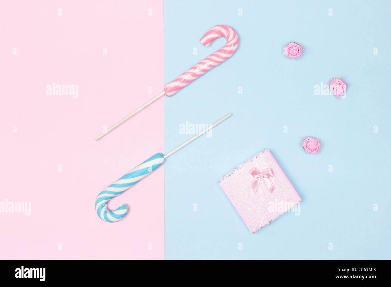 Due canne caramelle con scatola regalo su sfondo blu pastello e rosa. Vista dall'alto, disposizione piatta. Congratulazioni concetto minimo femminile Foto Stock
