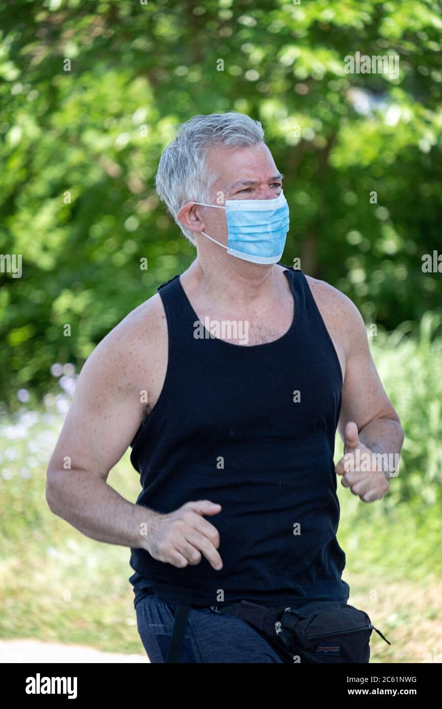 Un uomo di mezza età corre a Little Bay Park mentre indossa una maschera chirurgica. A Whitestone, Queens, New York City. Foto Stock