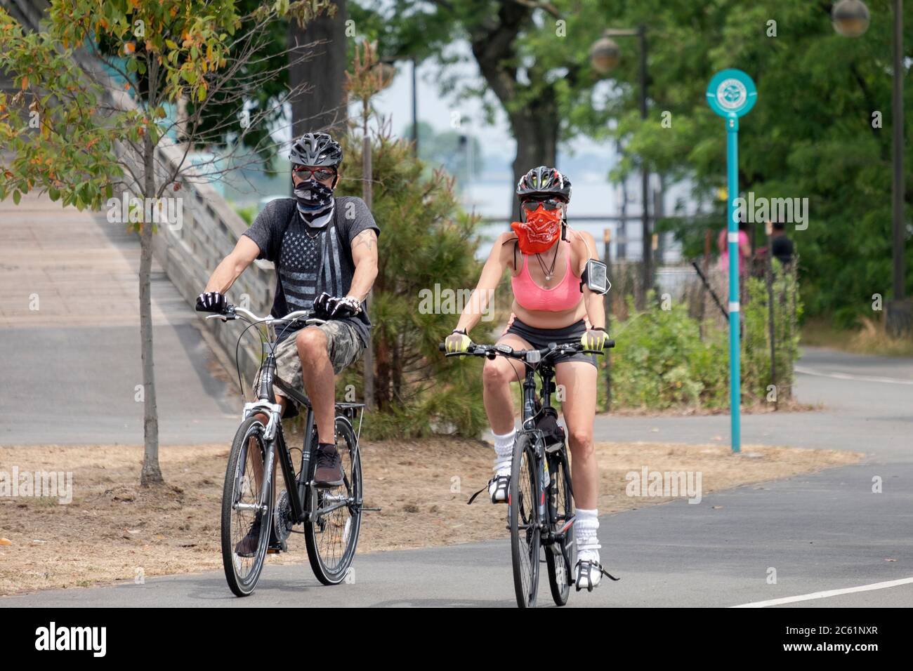 Una coppia in bicicletta su un sentiero vicino alla Marina di Bayside. Uno indossa una bandana e l'altro una sciarpa per il viso. A Bayside, Queens, New York City. Foto Stock