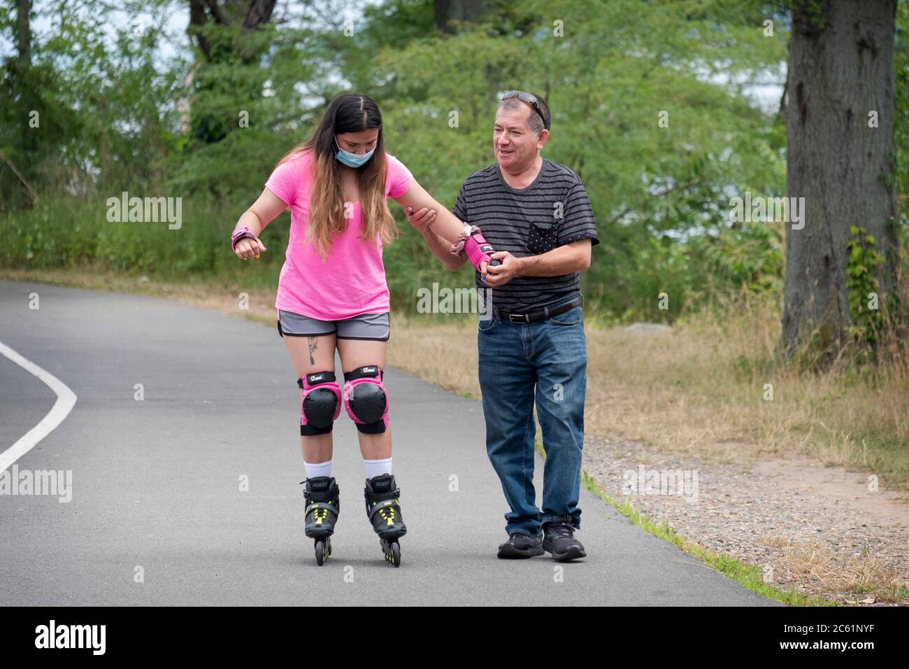 Un uomo di mezza età insegna a una giovane ragazza - probabilmente famiglia - come rollerblade. Vicino al Bayside Marina a Queens, New York City. Foto Stock