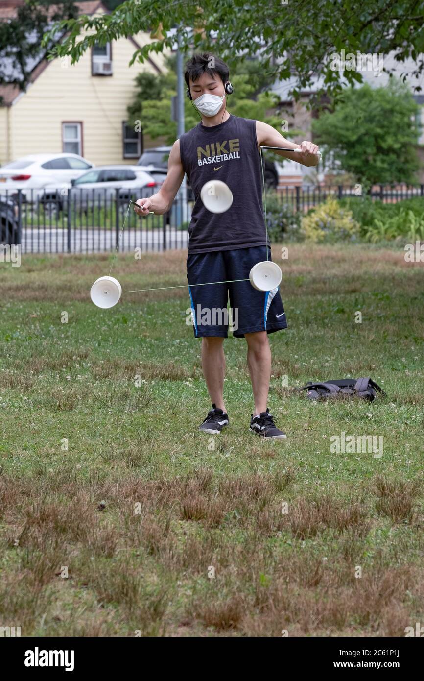 Un uomo asiatico americano che indossa una maschera chirurgica si esibisce su uno yoyo cinese chiamato Diablo. A Kissena Park, Flushing, New York City. Foto Stock