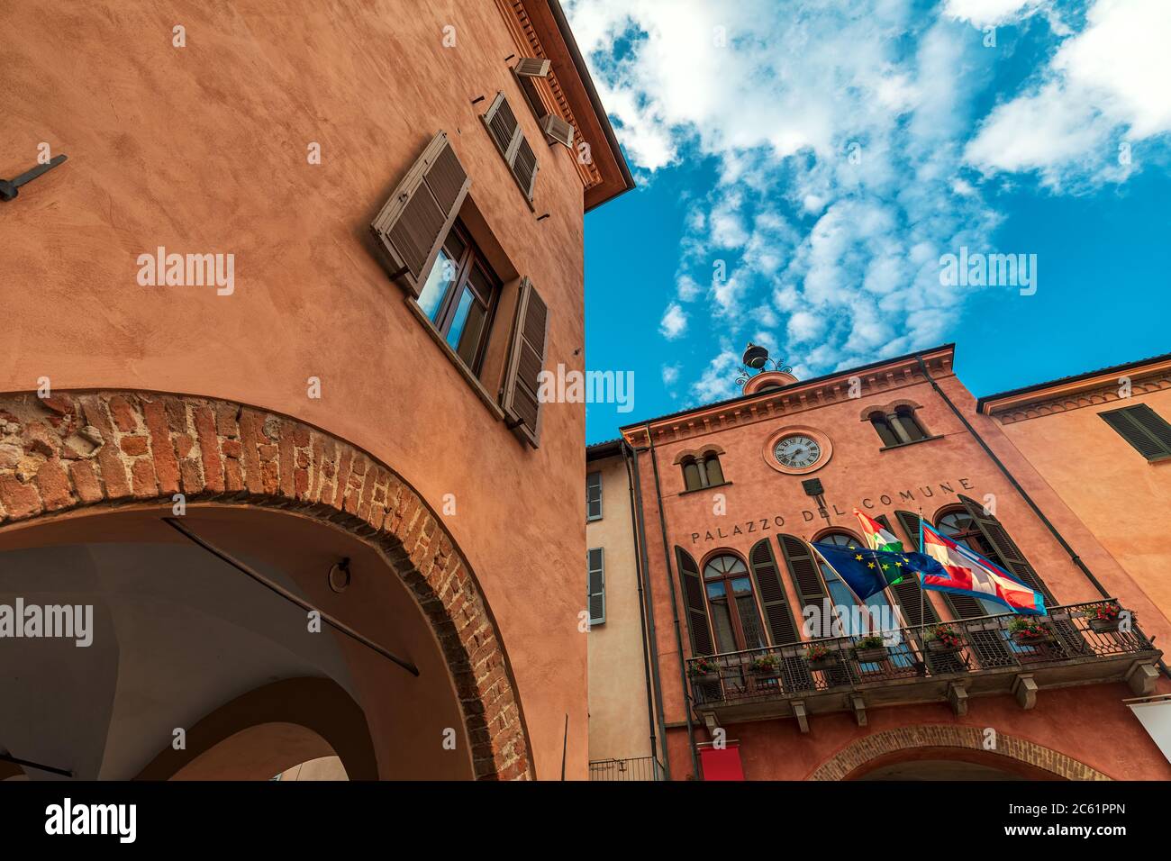 Antica casa storica e municipio con balcone, bandiere e orologio sotto il bel cielo di Alba, Piemonte, Italia settentrionale (vista ad angolo basso). Foto Stock