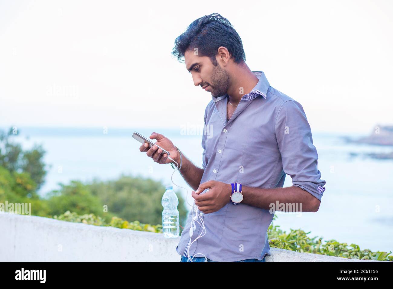 Profilo laterale di un uomo furioso che guarda le app su smartphone isolato all'aperto, sulla natura, mare su sfondo Foto Stock
