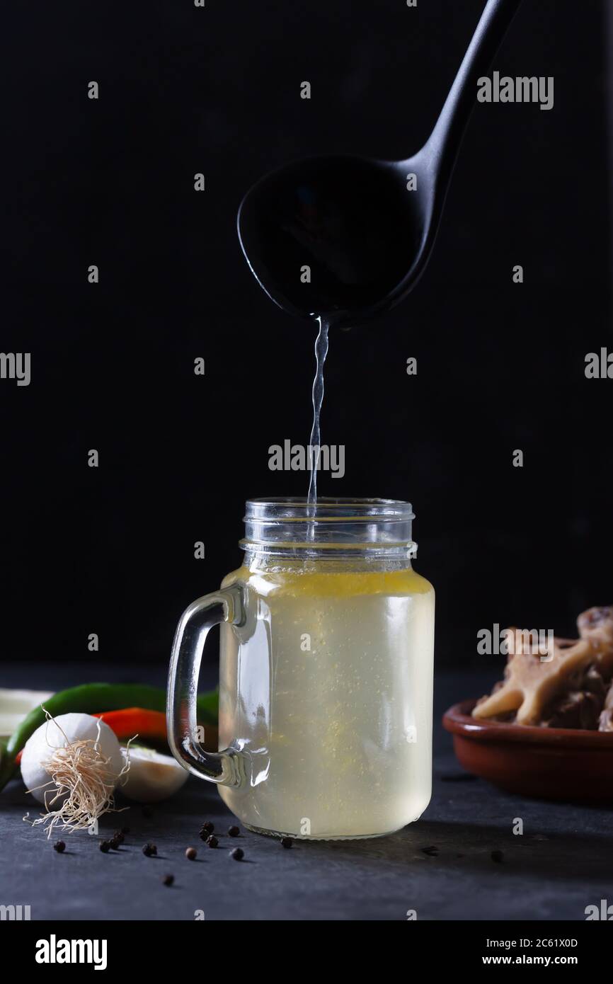 Versare brodo di manzo in casa in vetro vasetto di conservazione su sfondo nero Foto Stock