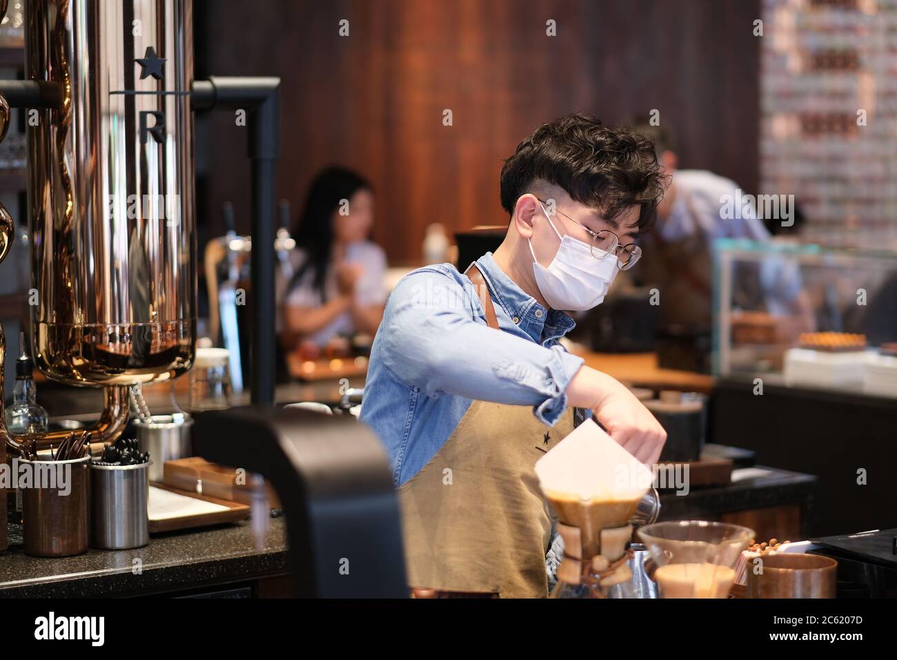 primo piano impiegato indossando maschera viso per evitare covid-19 coronavirus, lavorando in caffetteria Foto Stock