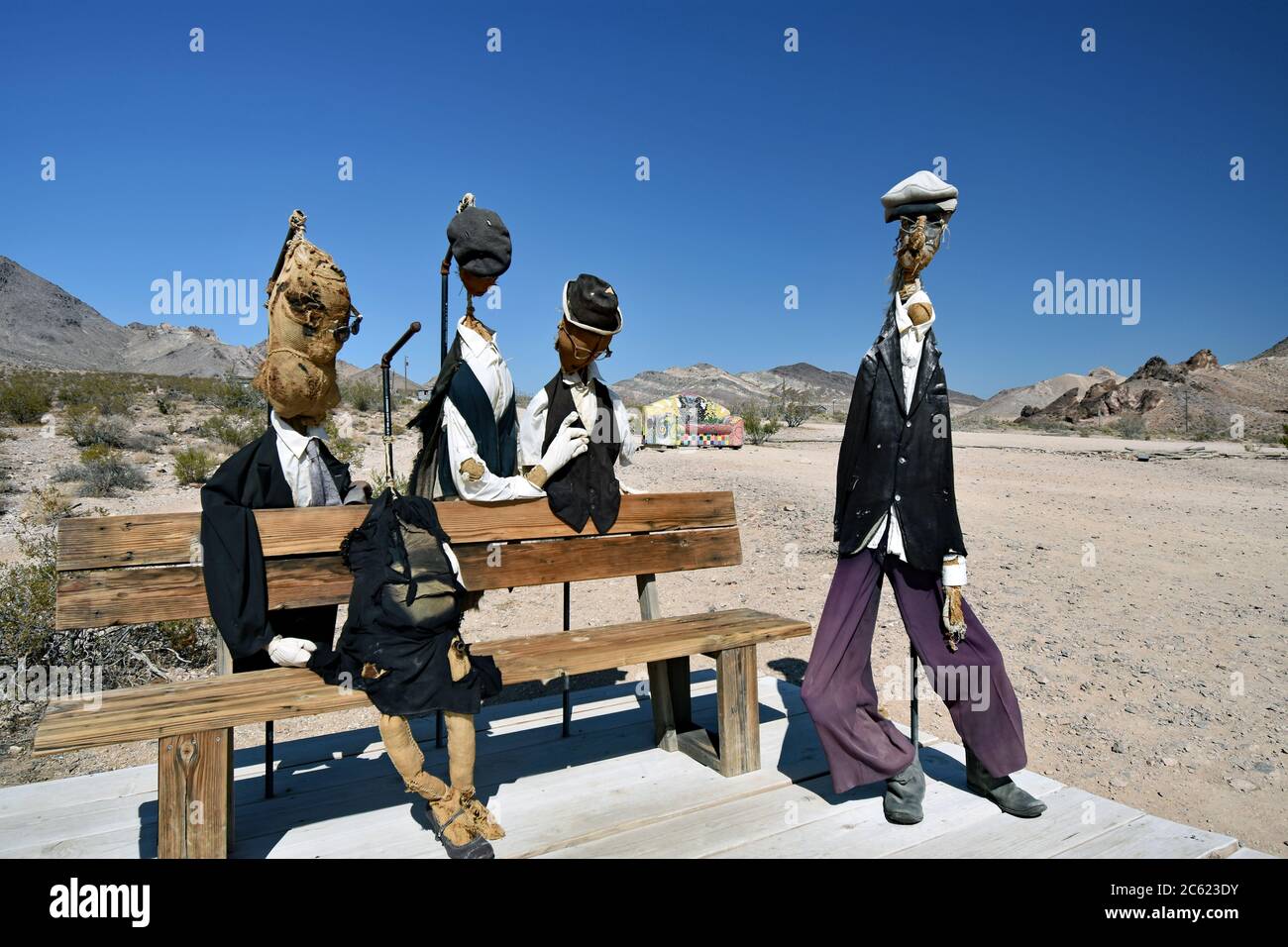 Quattro sculture di burlap ripiene di persone intorno a una panchina nel deserto. Intemperie danneggiate. Divano/divano a mosaico dietro. Museo all'aperto GOLDWELL, Nevada Foto Stock