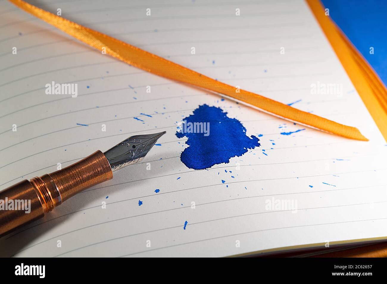 Una penna fontana di rame si scheggia su un notebook con legature arancioni e nastro di inchiostro blu Foto Stock