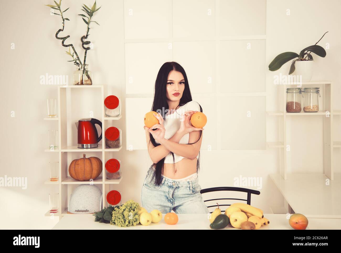 Calzata sportiva che tiene l'arancia vicino a frutta, verdura e metro a nastro su tavola da cucina, dieta per contare le calorie. Foto Stock