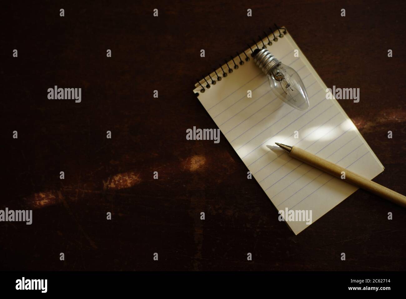 Notebook con penna e lampadina su un tavolo di legno scuro. Spazio di copia. Foto Stock