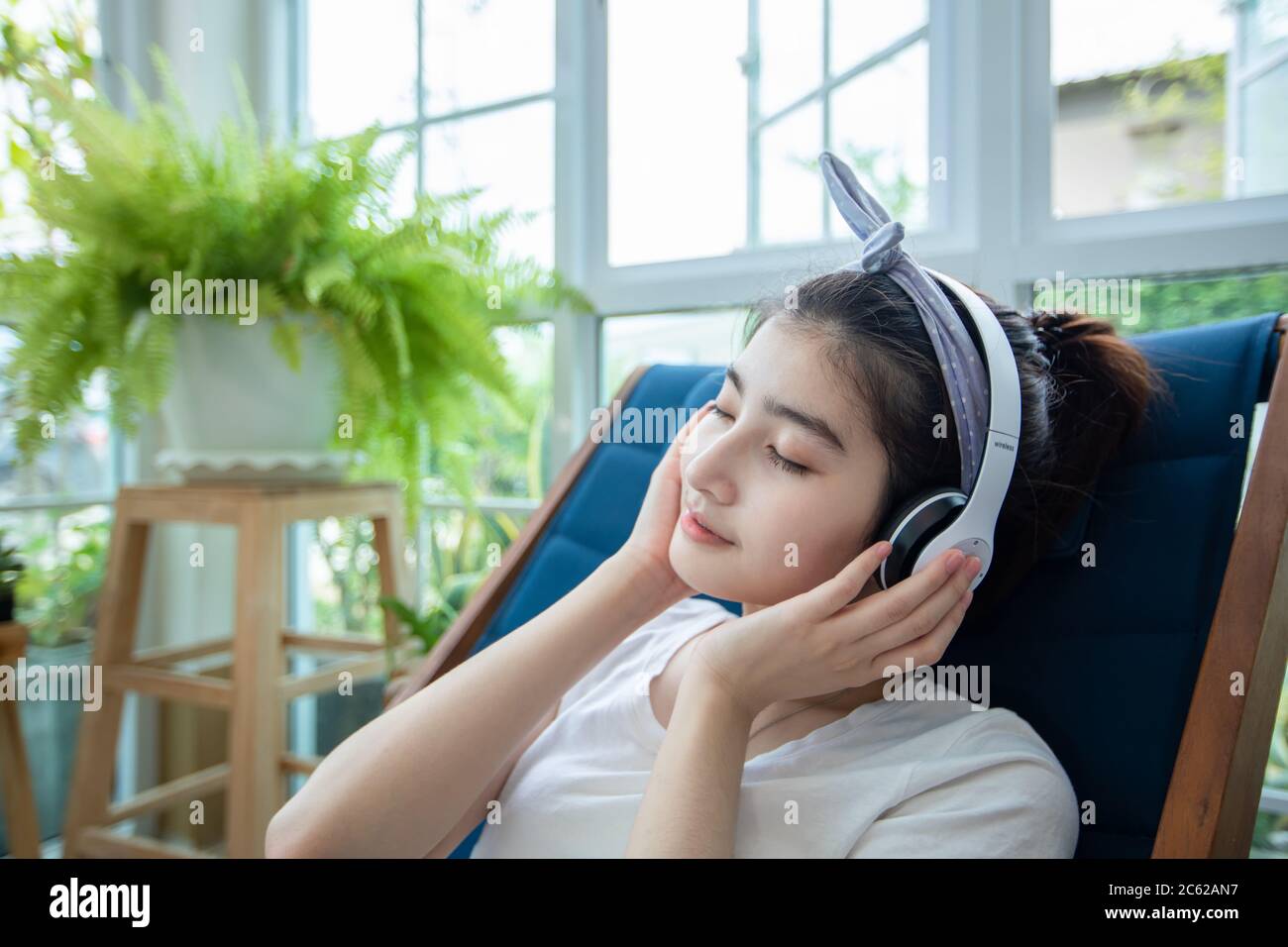 Belle donne asiatiche indossare cuffie e utilizzare un computer portatile per lavorare e ascoltare musica in giardino a casa in una giornata rilassante. Foto Stock