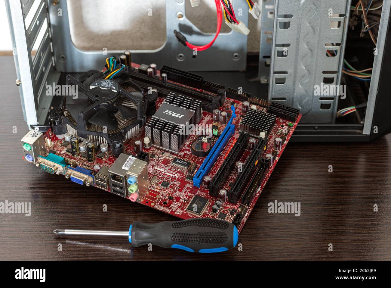 Ucraina - 25 aprile 2020: Scheda madre del computer scollegata e cacciavite Phillips vicino al case su sfondo marrone. Componenti hardware, backgr Foto Stock