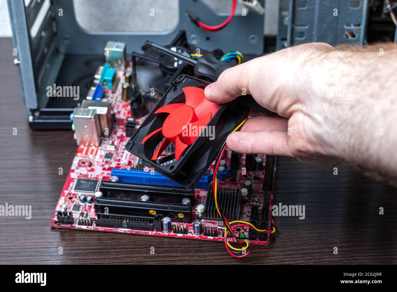 Il nuovo radiatore PCU nell'uomo consegna la scheda madre scollegata vicino al case sulla superficie marrone. Vista ravvicinata Foto Stock