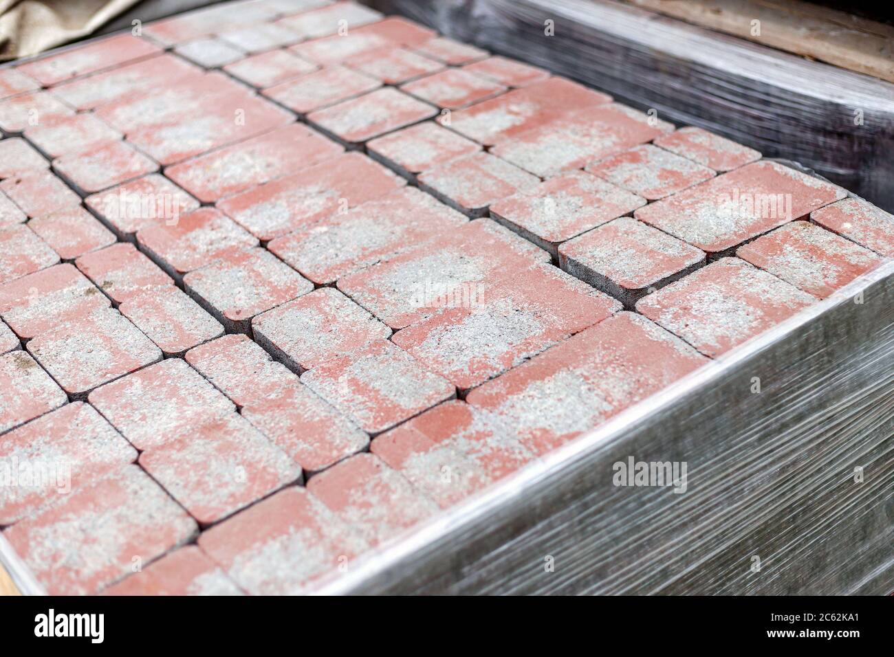 Primo piano di nuovi sassi rossi dell'asfaltatrice in pallet fissati con avvolgimento elastico. Blocca la struttura, lo sfondo, il materiale per la pavimentazione Foto Stock