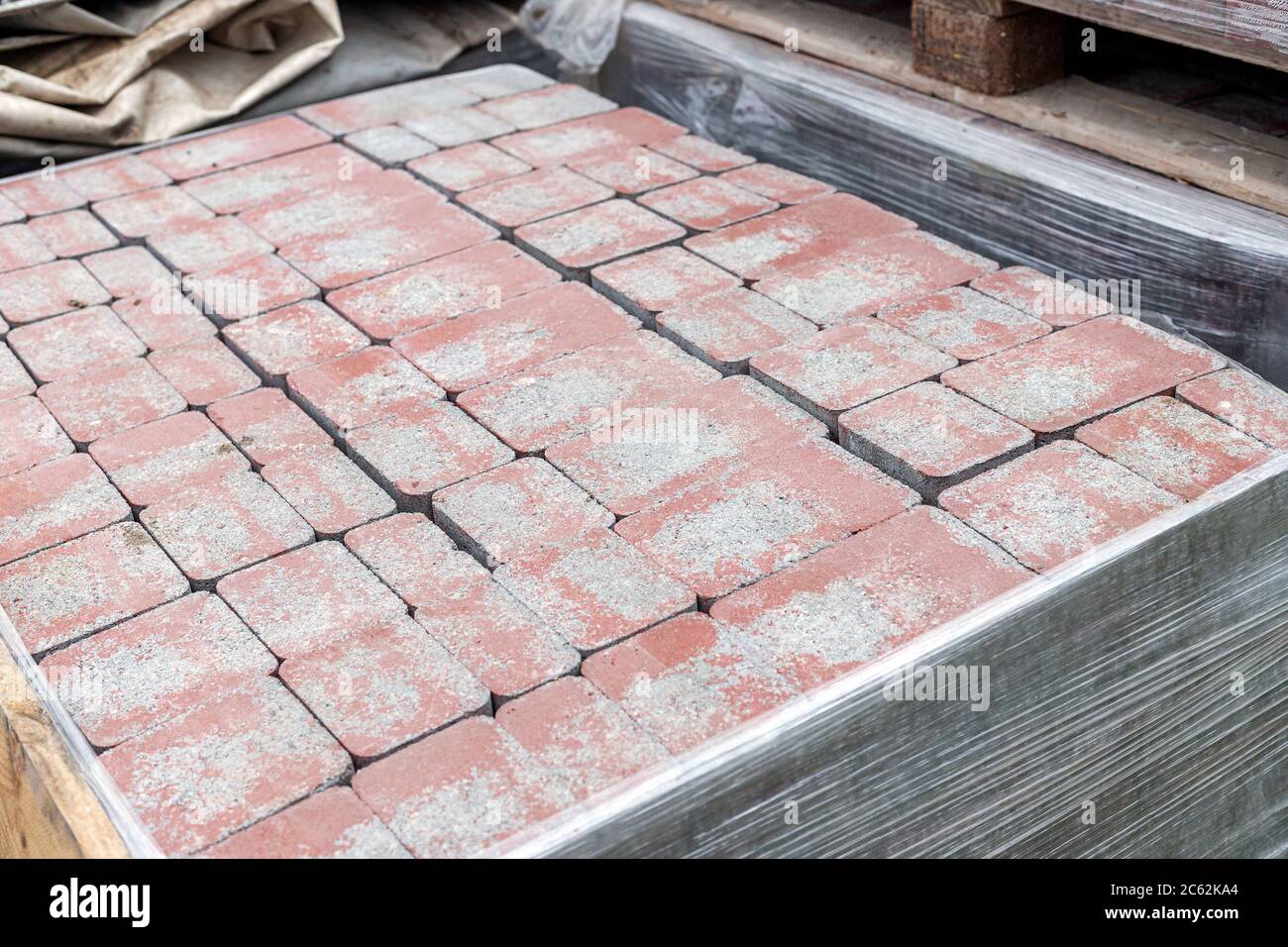 Primo piano di un palo di pietre per asfaltatrice nuove e rosse in pallet fissato con avvolgimento elastico. Blocca la struttura, lo sfondo, il materiale da costruzione per la pavimentazione Foto Stock