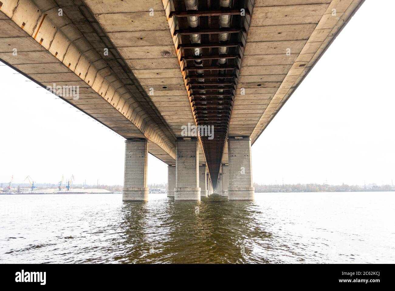 Vista dal basso delle colonne grigie in cemento del ponte sul fiume. Ponte moli, cielo riflessione sull'acqua, prospettiva, sfondo Foto Stock