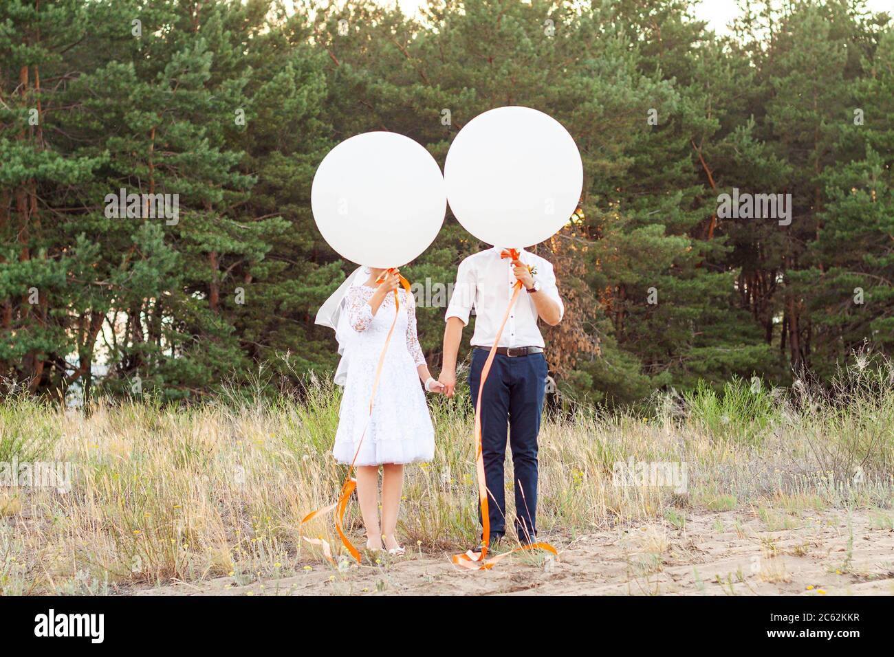 Sposa e sposo che tengono grandi berline di elio bianco con nastri di arancio nella foresta. Concetto di idea di matrimonio, sfondo Foto Stock