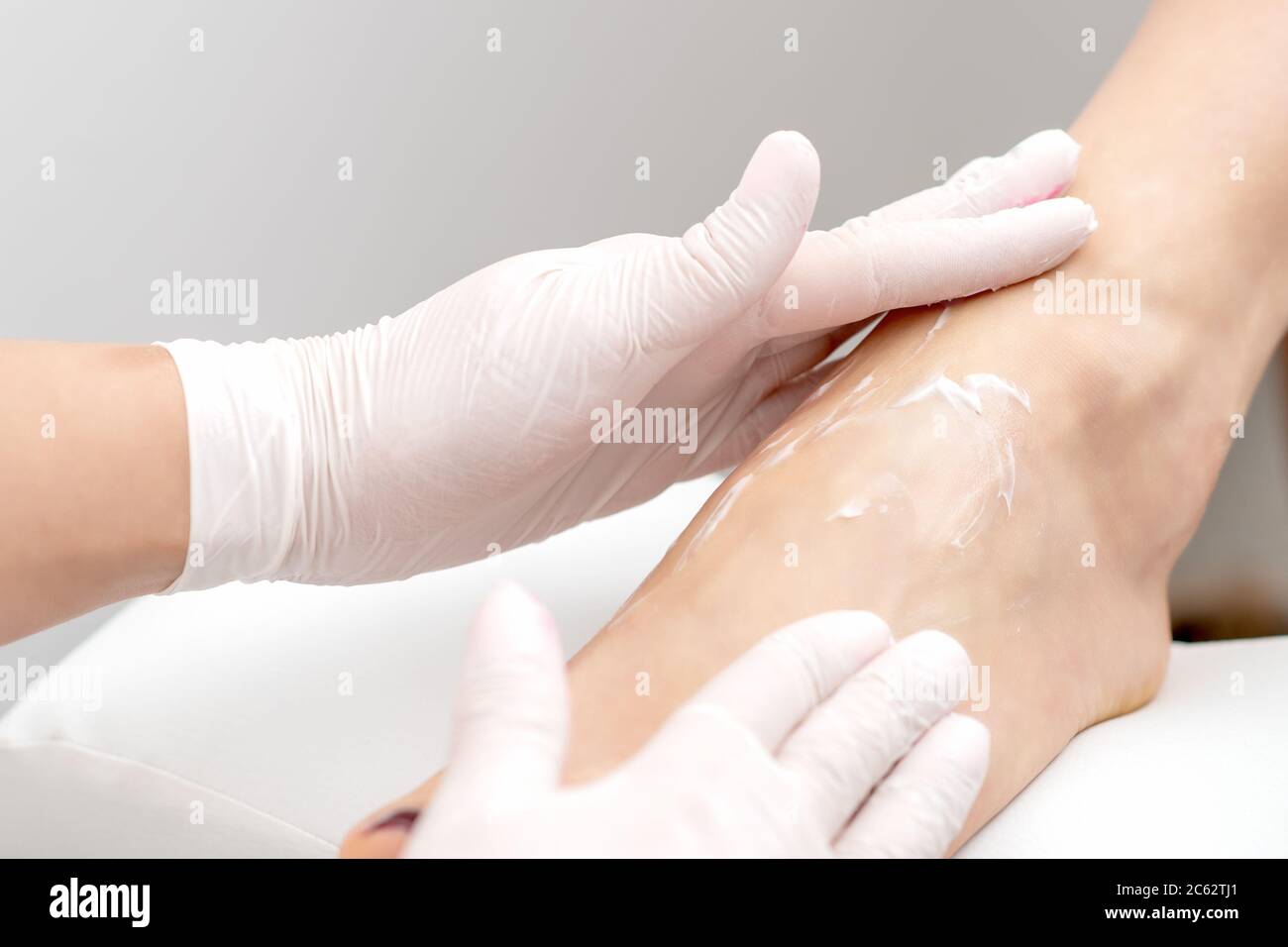 Mani umane in guanti protettivi facendo massaggio ai piedi con crema  idratante o peeling in salone di bellezza Foto stock - Alamy