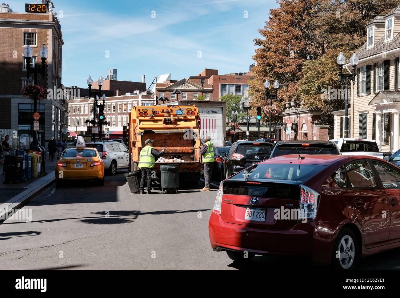 Il camion di raccolta dei rifiuti ha visto i bidoni di raccolta in una strada trafficata con i rifiuti uomini visti sul retro del camion. Foto Stock