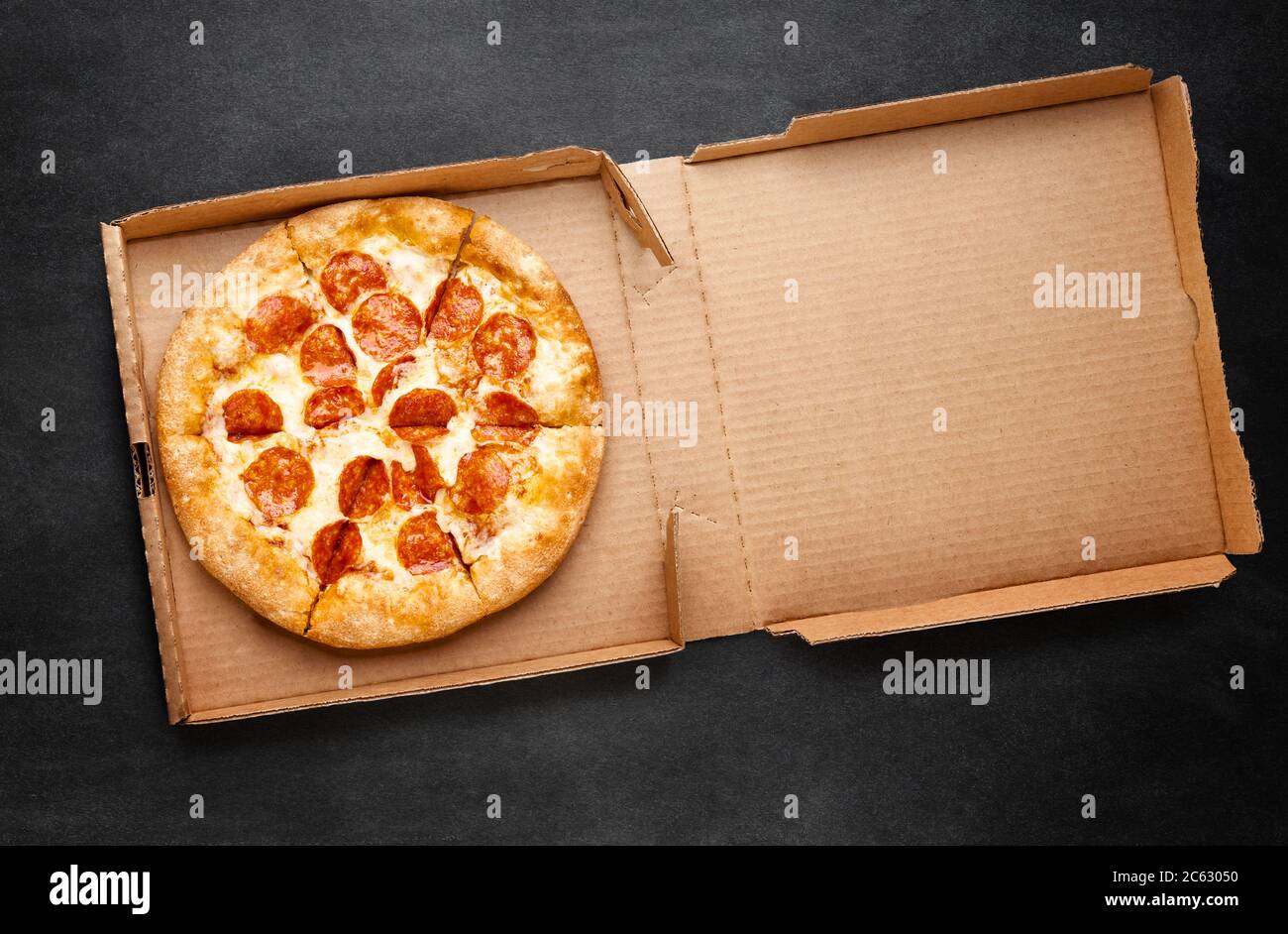 Pizza in una scatola di cartone su una lavagna scura. Spazio per il testo. Vista dall'alto del pacchetto pizza. Consegna pizza. Foto Stock