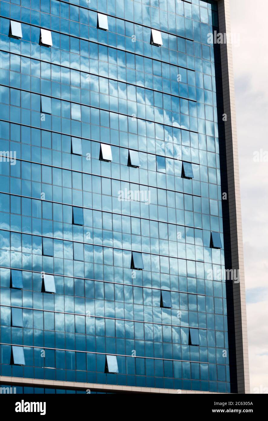Il cielo blu e le nuvole riflettono o riflettono sulla moderna facciata dell'edificio in vetro blu dell'ufficio come concetto architettonico simmetrico. Foto Stock