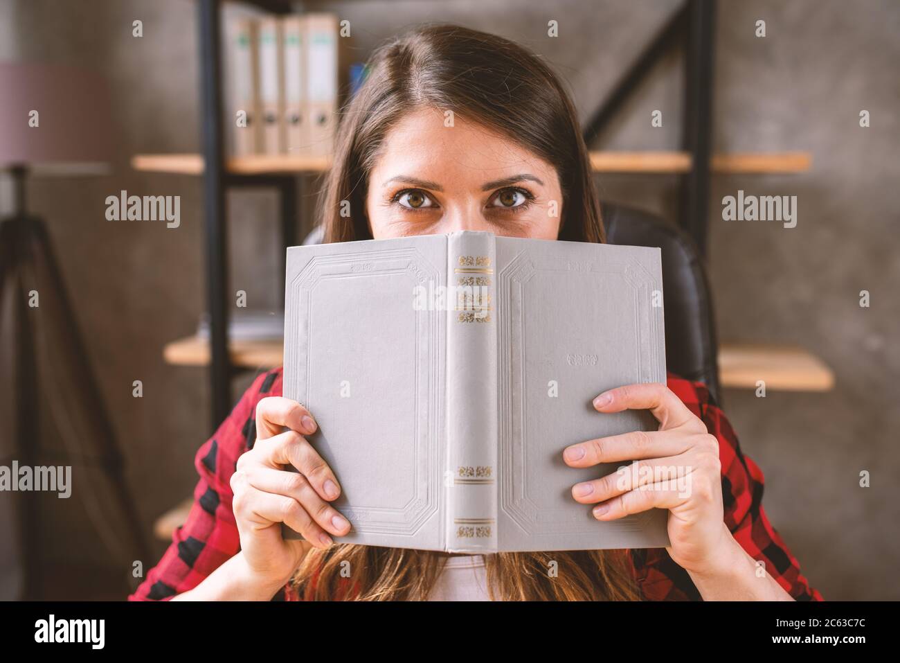 Ragazza è nascosto dietro un libro grigio. Concetto di curiosità Foto Stock