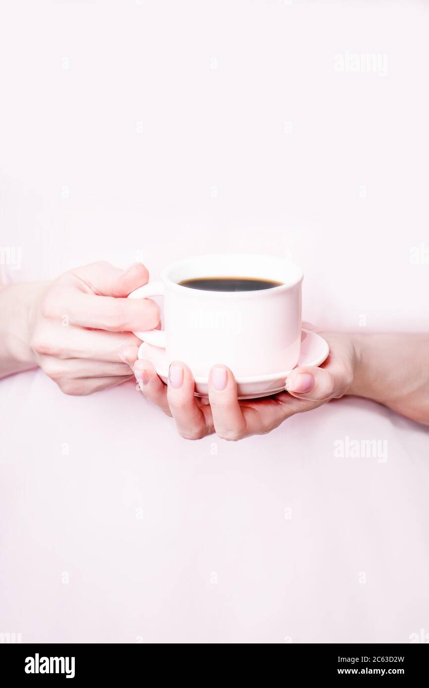 Mani femminili che tengono una tazza rosa di caffè nero su sfondo rosa. Spazio di copia Foto Stock