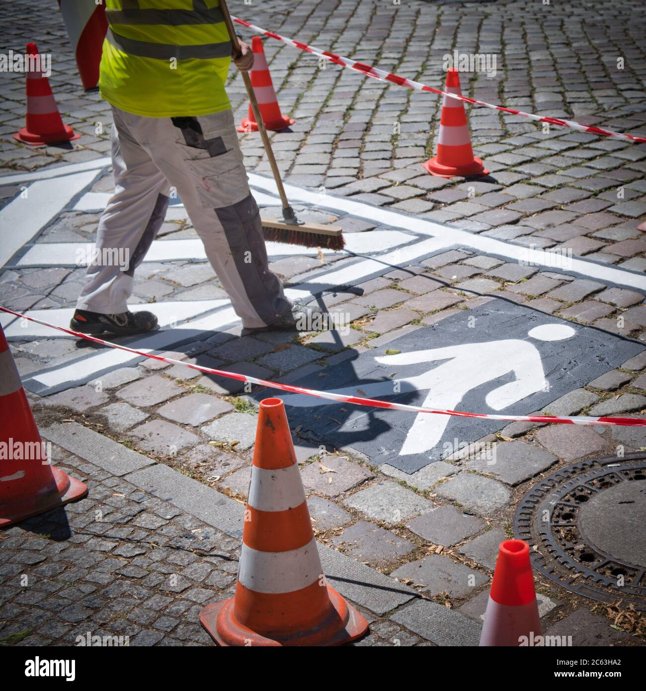 Closeup di un operaio stradale preparazione di un pittogramma bianco in una strada con conesa arancione e nastro per scherma per la sicurezza (quadrato) Foto Stock