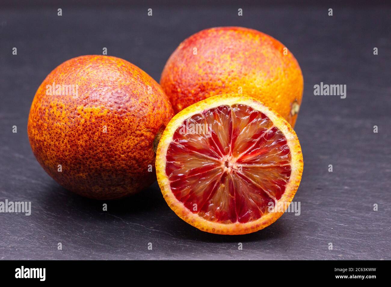 Piena e metà delle arance rosse isolate su sfondo scisto nero. Le citruse giacciono su una superficie di pietra Foto Stock