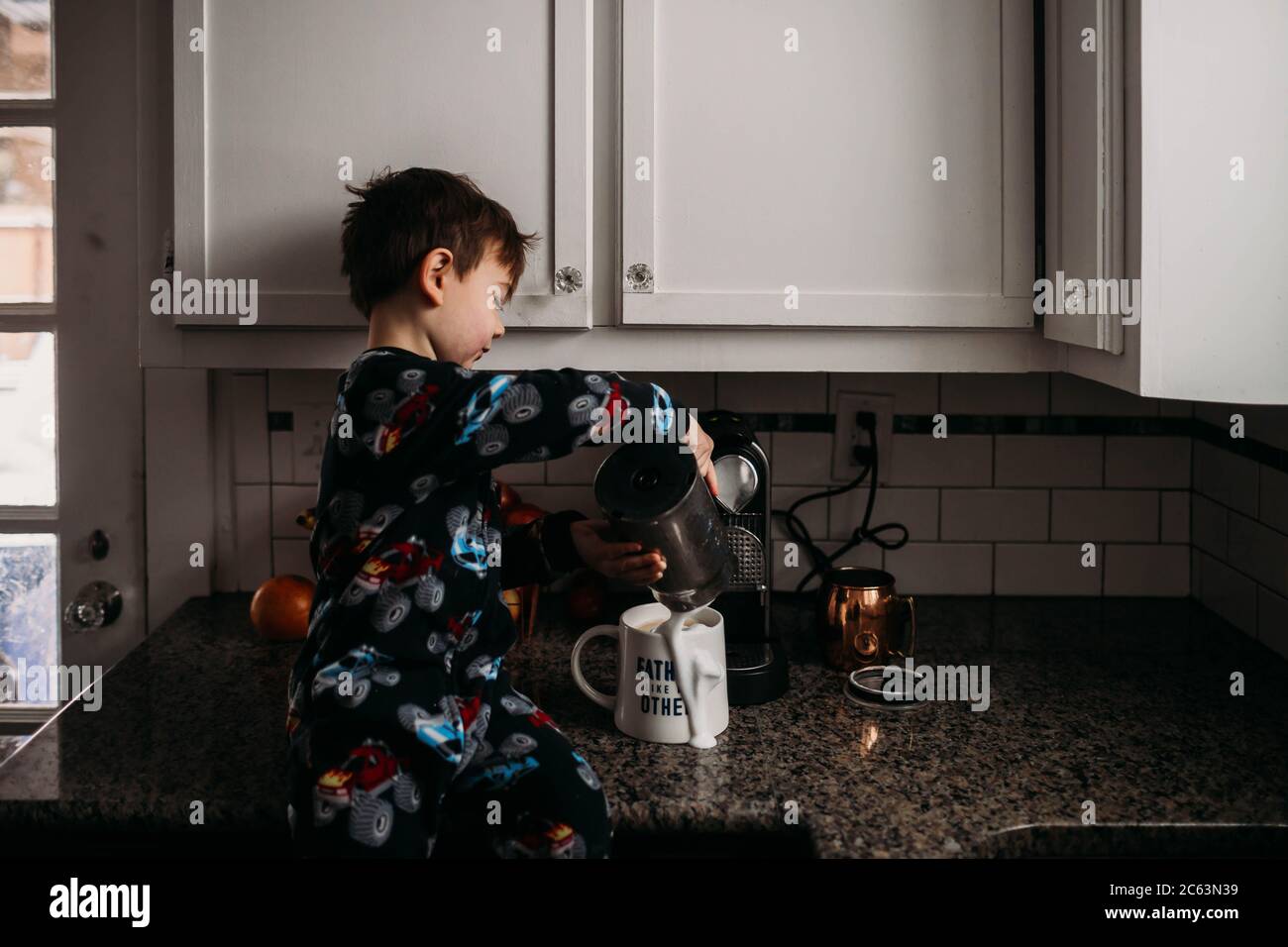Ragazzo seduto sul coutter della cucina che versava il latte sul caffè tazza Foto Stock
