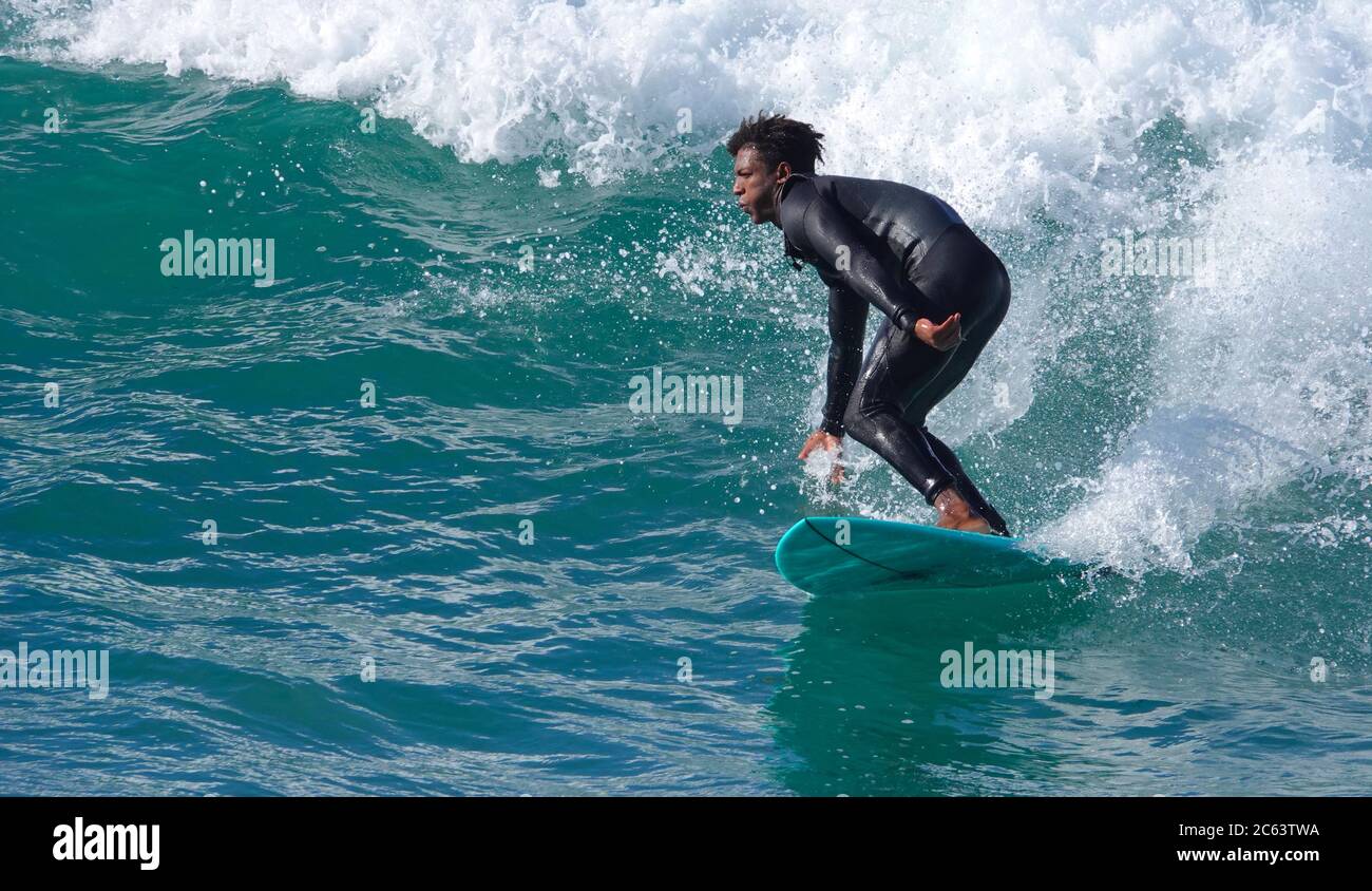 Teenage boy surfer (afroamericano) a cavallo di un'onda su tavola blu Foto Stock