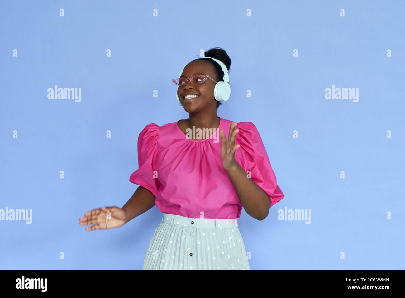 Donna africana sorridente che indossa cuffie e occhiali da sole rosa che ballano sul lilla. Foto Stock