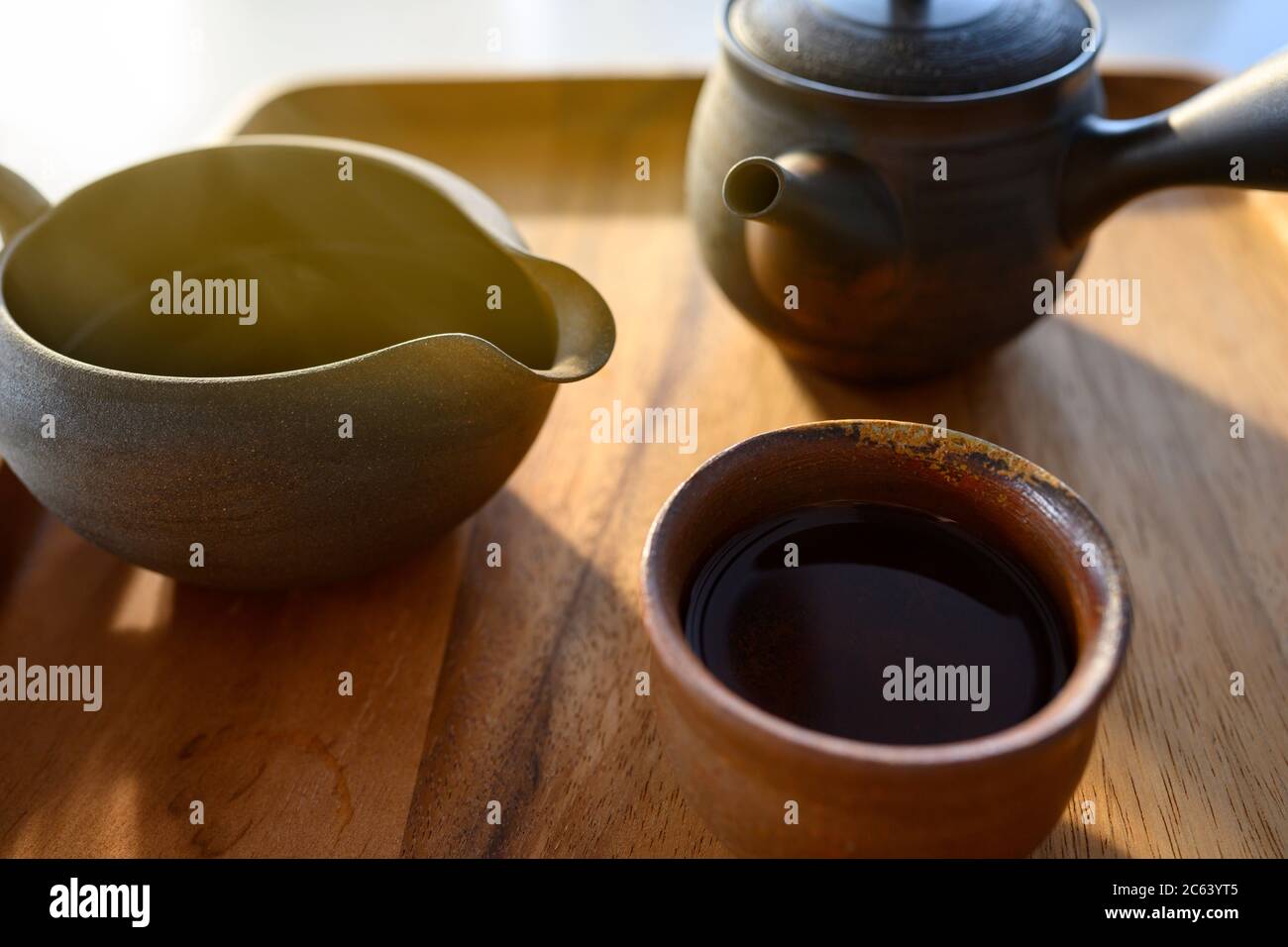 Set da tè in argilla marrone scuro in stile asiatico con vassoio di legno, chiaro al mattino dalla finestra Foto Stock