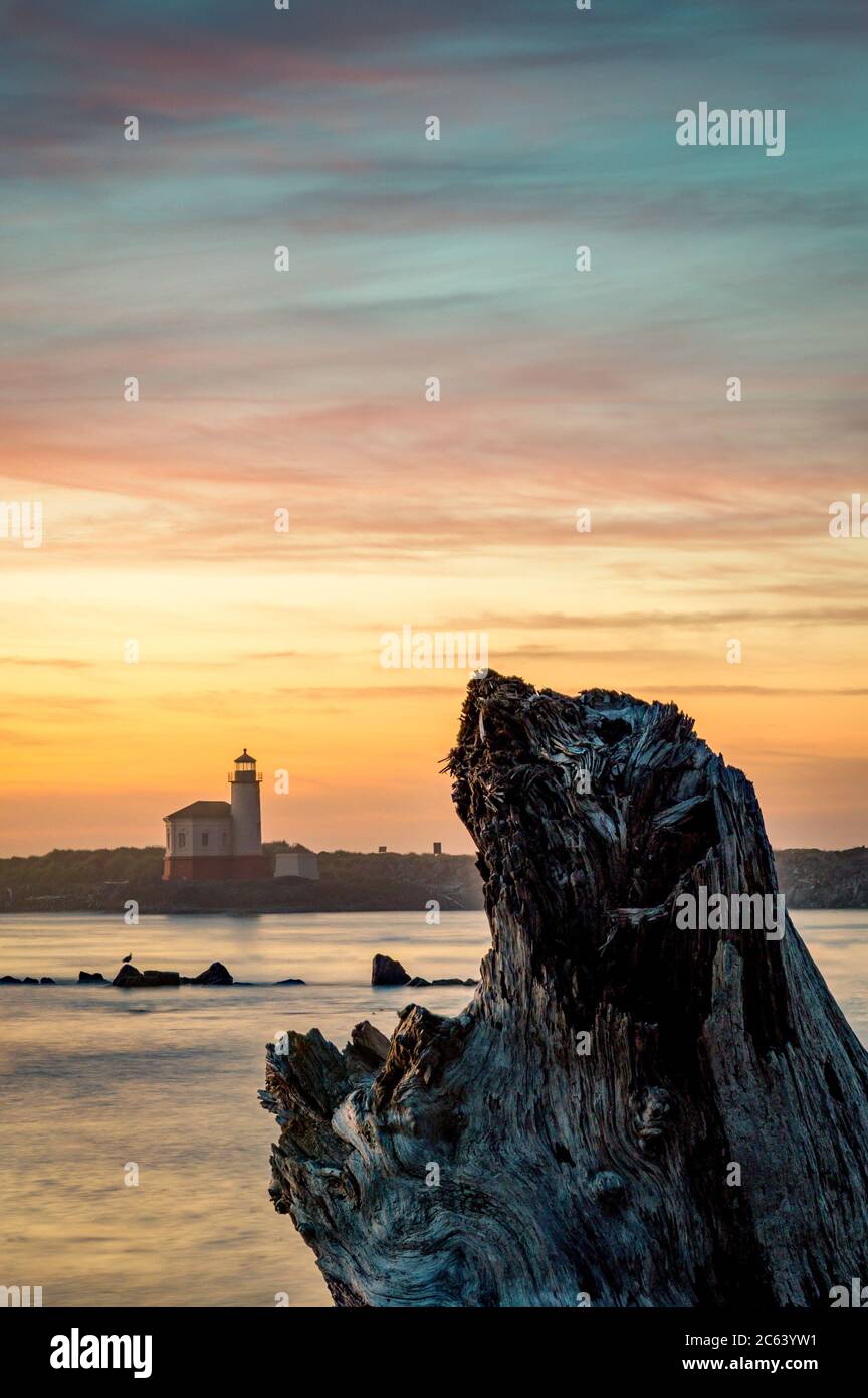 Faro visto attraverso il fiume al tramonto con driftwood, immagine verticale Foto Stock