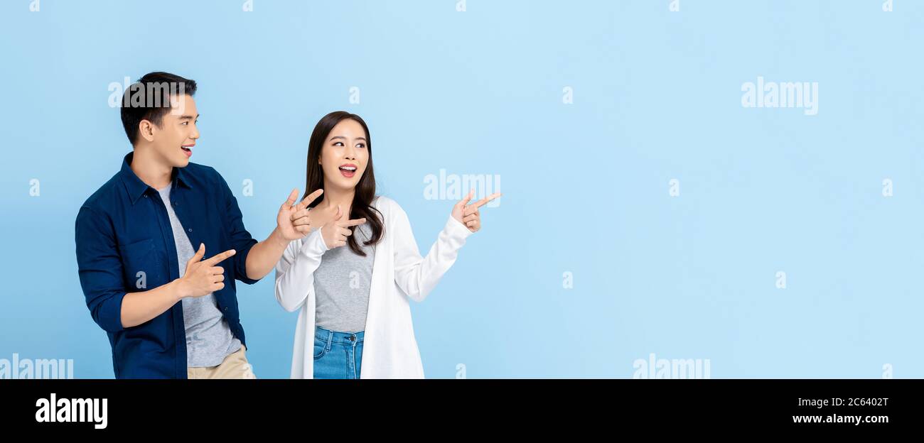 Sorridente eccitati turisti asiatici coppia indicando la mano a spazio vuoto su isolato sfondo blu chiaro banner Foto Stock