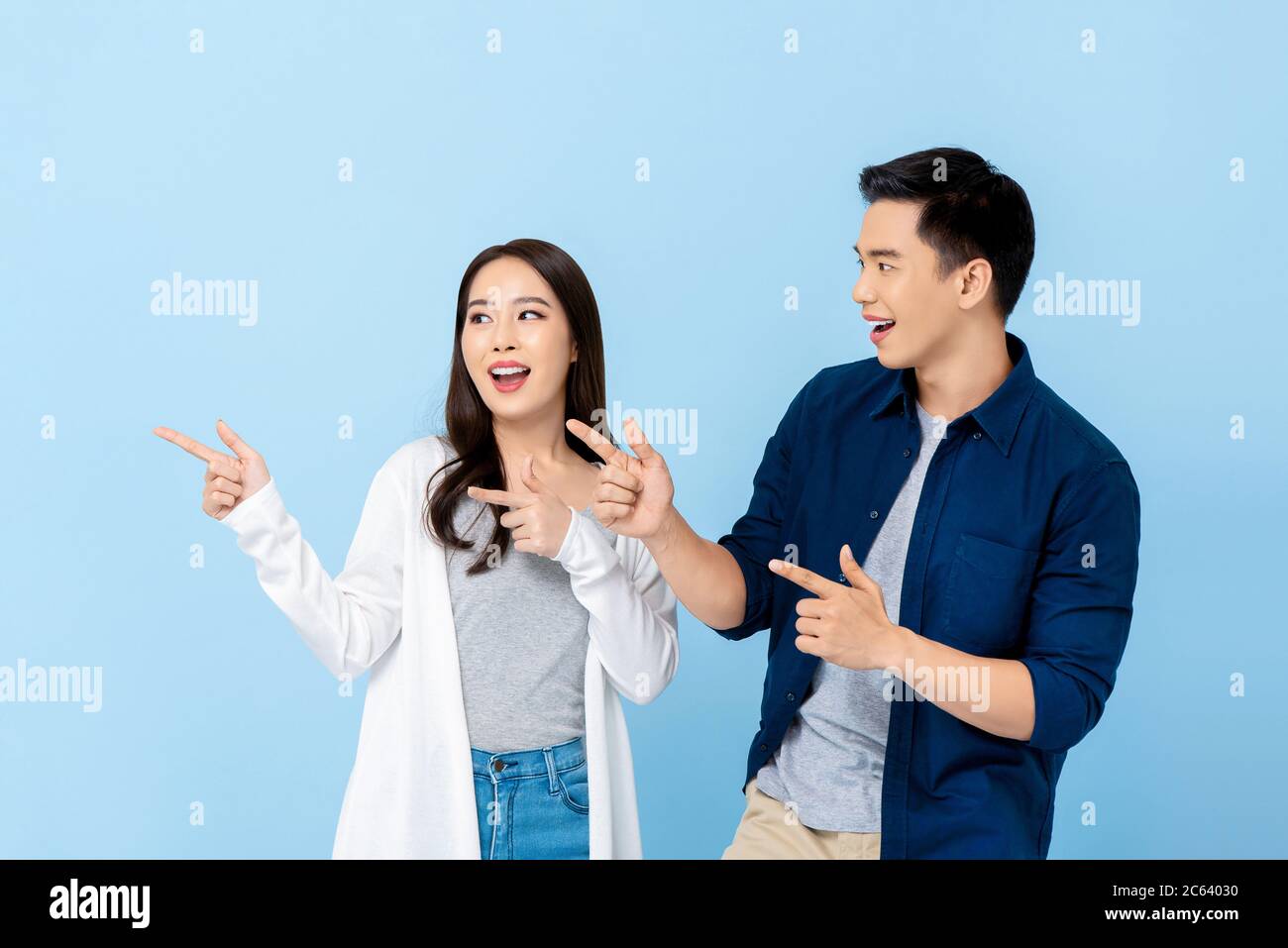 Sorridente eccitati turisti asiatici coppia indicando la mano a spazio vuoto su isolato sfondo azzurro Foto Stock