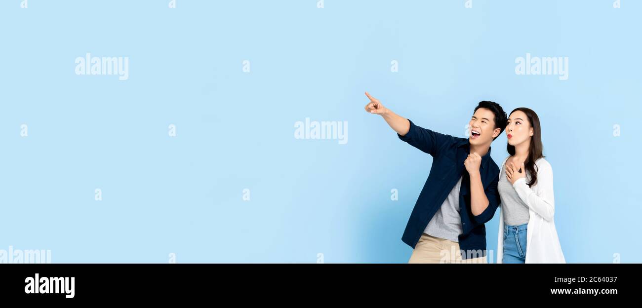 Stupito coppia di turisti asiatici eccitati che puntano la mano a spazio vuoto su isolato sfondo blu chiaro banner Foto Stock