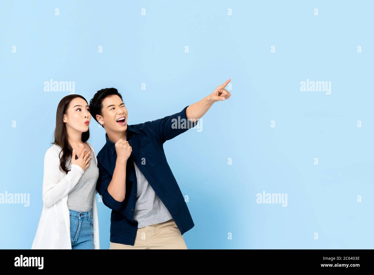 Stupito eccitati turisti asiatici coppia che puntano la mano a spazio vuoto su isolato sfondo azzurro Foto Stock