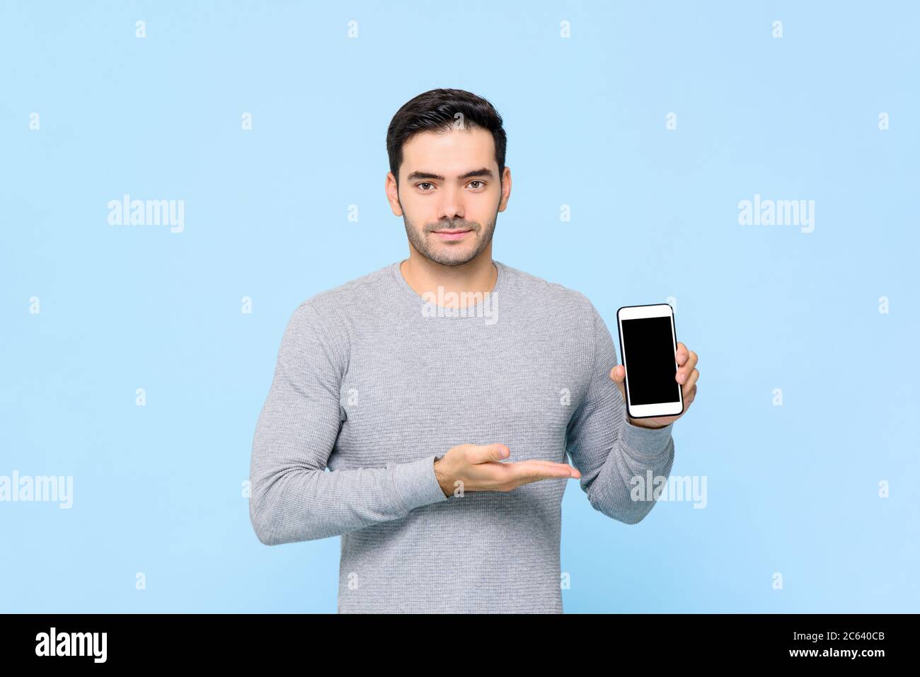 Bell'uomo caucasico che mostra il telefono cellulare con schermo vuoto isolato su sfondo azzurro Foto Stock