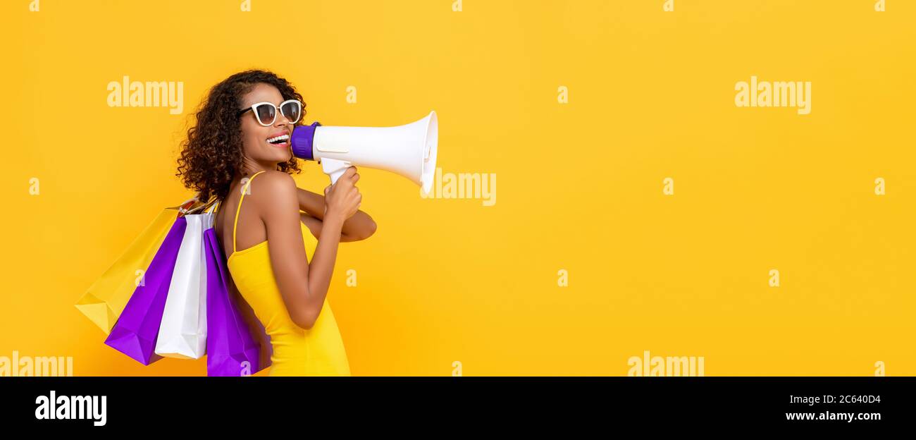 Felice bella donna con borse e megafono shopping su isolato sfondo colorato giallo banner per la vendita e concetti di sconto Foto Stock